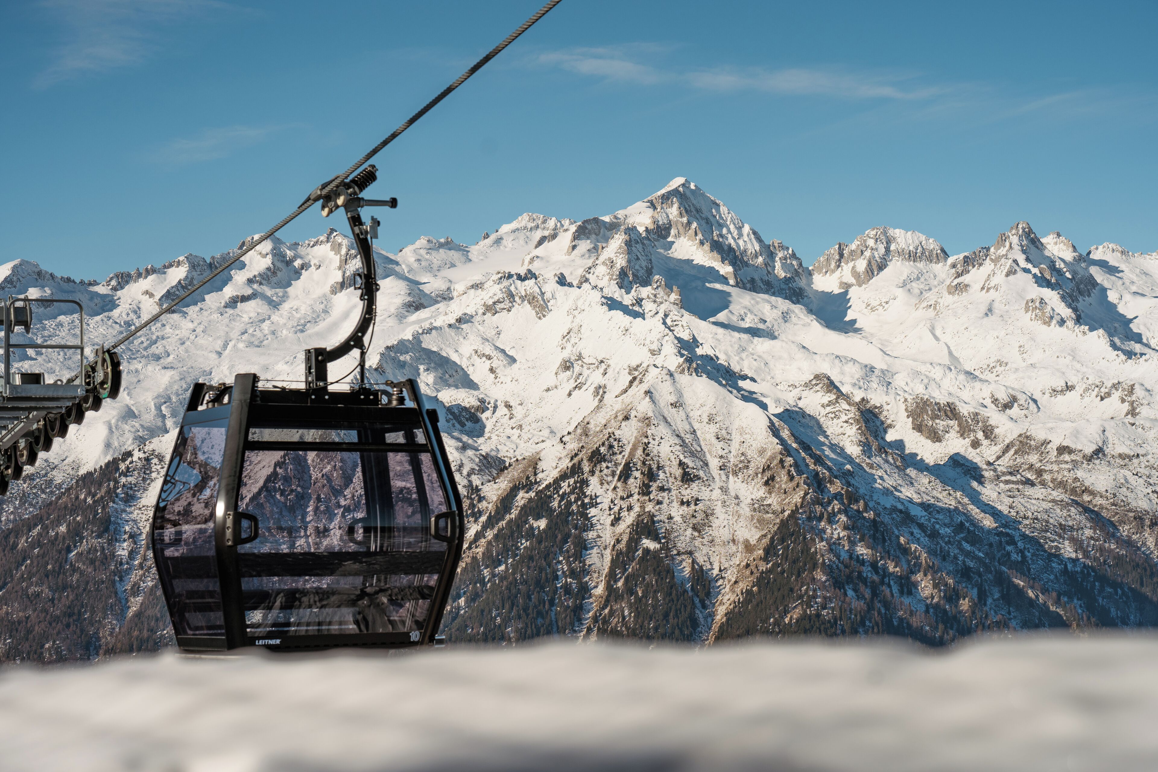 A cable car ascending a snow-covered mountain with a clear sky.