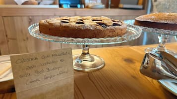 Una vetrina di panetteria con una torta su un piedistallo di vetro, un cartello con scritta a mano e un tavolo di legno.