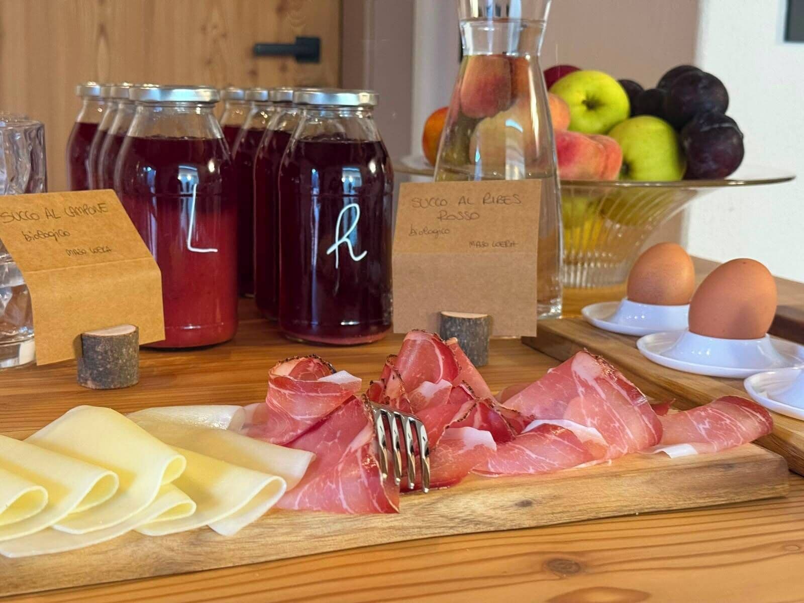 Ein Holztisch mit verschiedenen Speisen, darunter Wurstwaren, Käse und eine Schüssel Obst.
