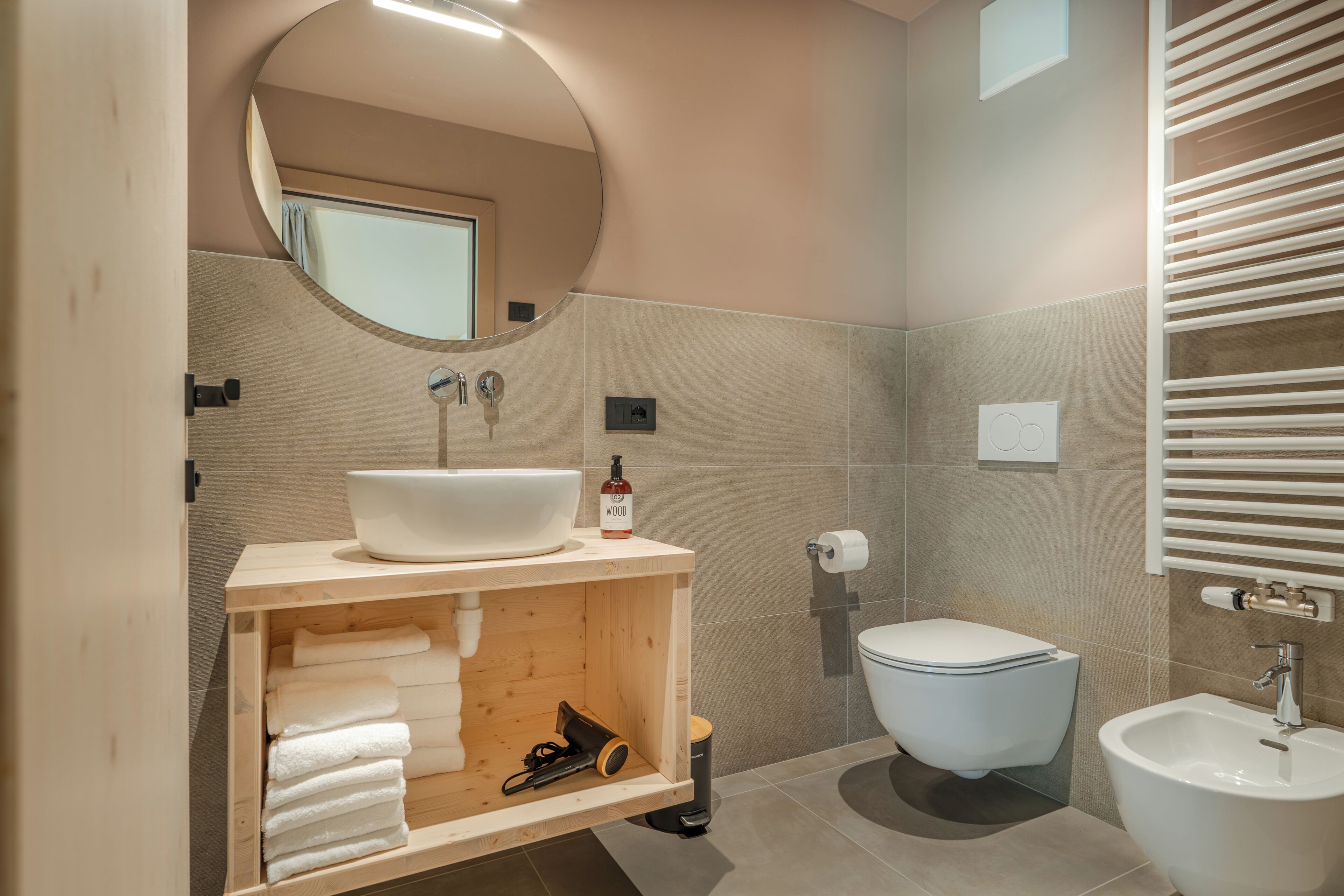Un baño moderno con un espejo redondo, un lavamanos blanco, un inodoro y un bidé.