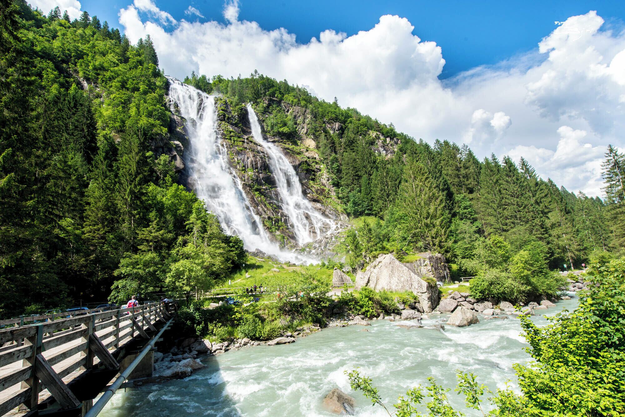 A waterfall cascading down a forested hillside with a river below.