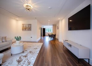 A modern living room with a sofa, a coffee table with a plant, a dining area with chairs, and a TV mounted on the wall. - 157 Vansittart Road (Leeds)