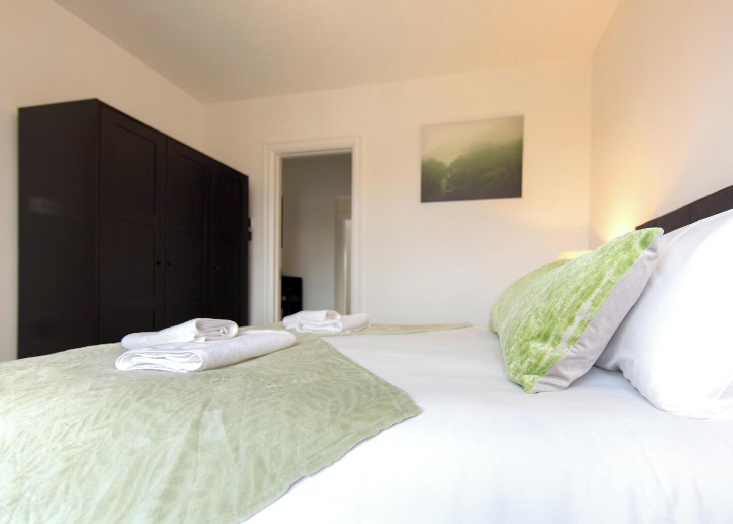 A hotel room with a bed, a dark wardrobe, and a door leading to another room.
