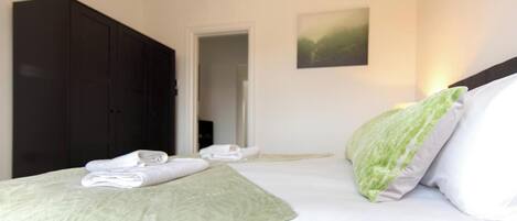 A hotel room with a bed, a dark wardrobe, and a door leading to another room.
