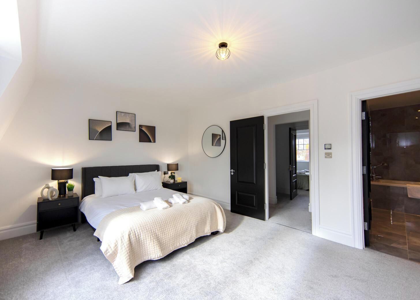 A bedroom with a bed, bedside tables, a nightstand, a mirror, and a door leading to a bathroom.