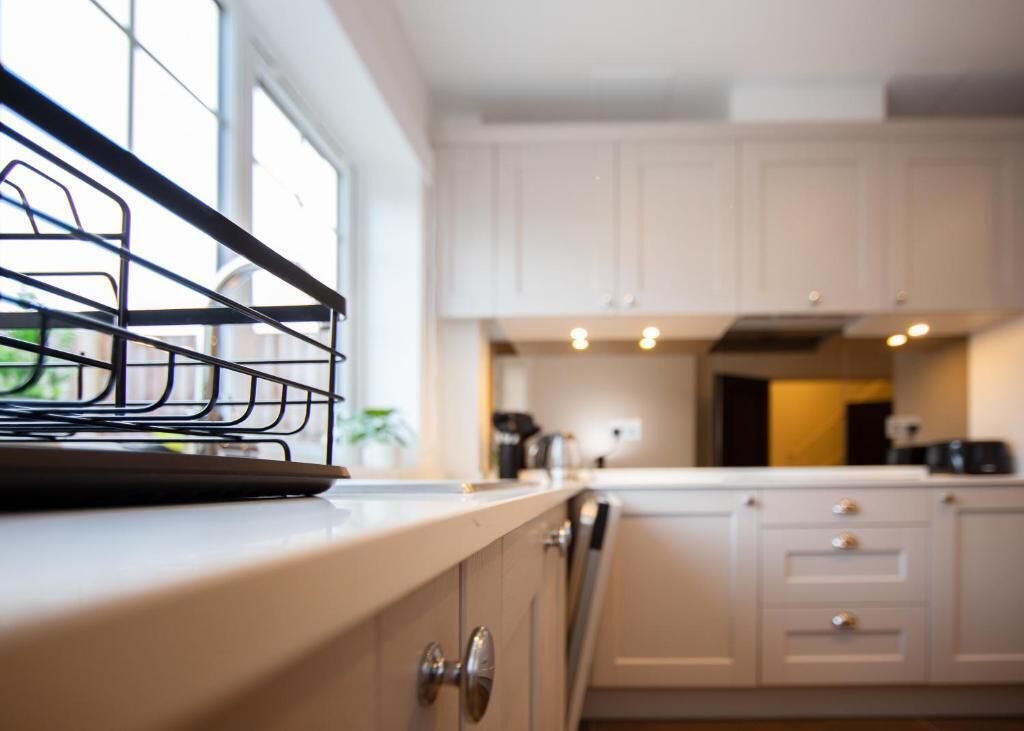 A kitchen with white cabinets, a window, and a metal rack on the counter.