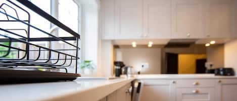Una cocina con armarios blancos, un ventanal y una estantería metálica en la encimera.