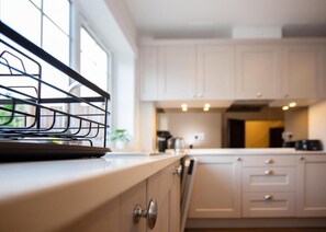 A kitchen with white cabinets, a window, and a metal rack on the counter. - 157 Vansittart Road (Leeds)