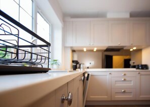 A kitchen with white cabinets, a black kitchen rack, and a window with a view of greenery. - 157 Vansittart Road (Windsor)