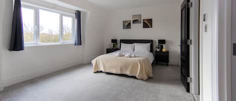 A bedroom with a bed, bedside tables, a window, and a door.