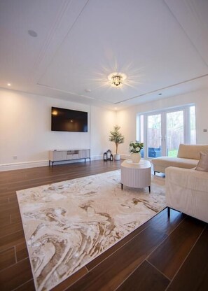 A spacious living room with a large window, a flat-screen TV mounted on the wall, a round coffee table, and a beige sofa. - 157 Vansittart Road (Windsor)