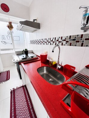 A modern kitchen with a red countertop, stainless steel sink, and a window with a view. - Cove retreat with 4 bedrooms, pool and comfort. (Guarujá)