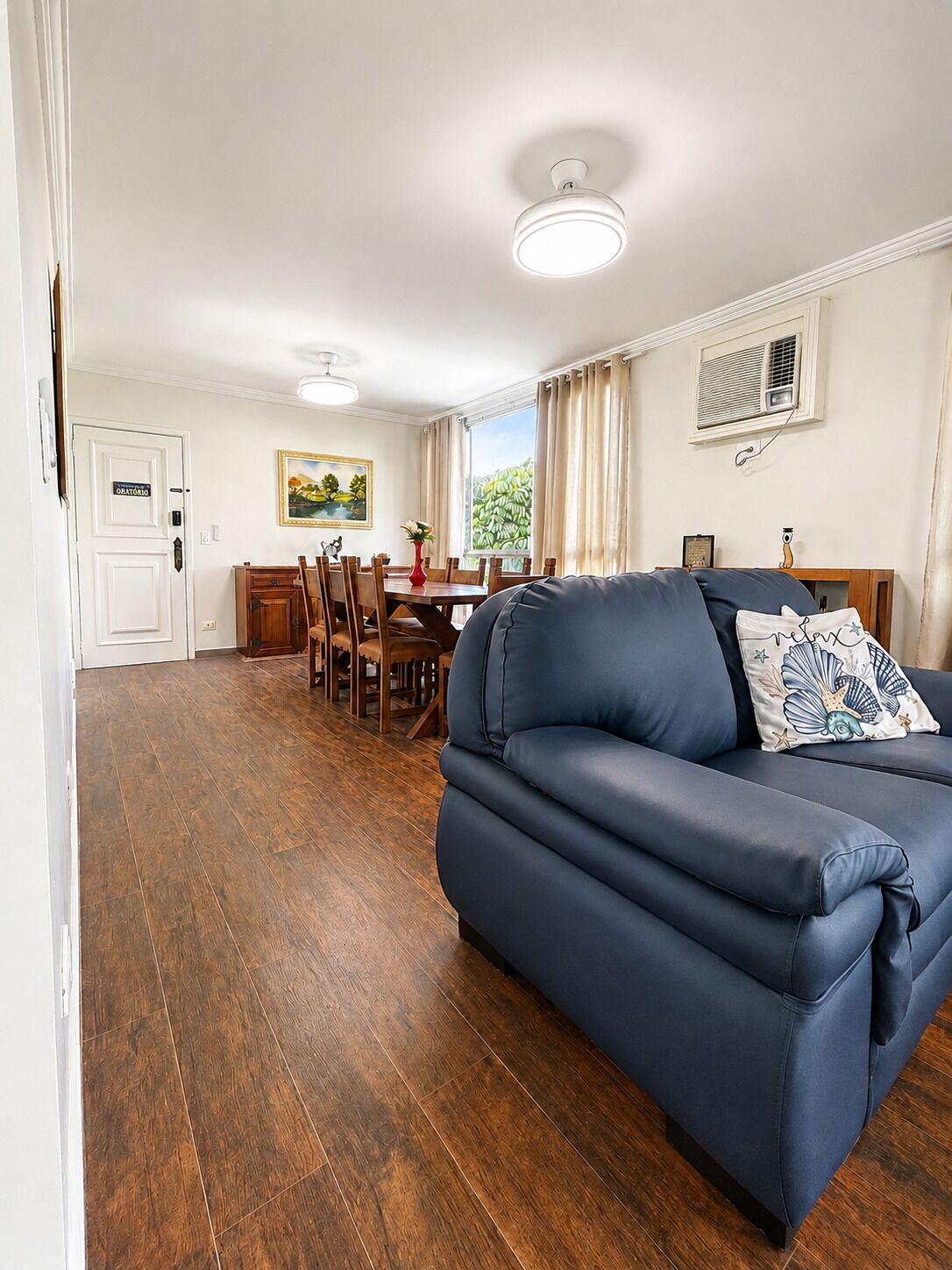 Un salón con un sofá azul oscuro, una zona de comedor con muebles de madera y un cuadro en la pared.