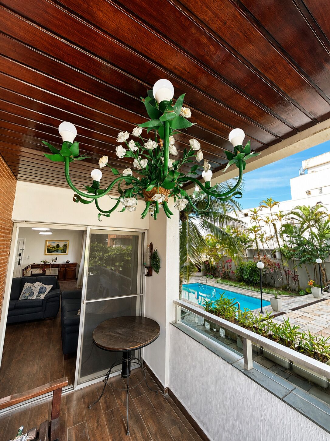 A balcony with a pool, a dining area, and a living room with a sofa and a table.