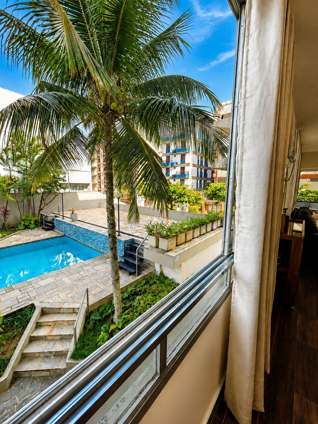 Un balcon avec vue sur une piscine, des palmiers et un immeuble à plusieurs étages.
