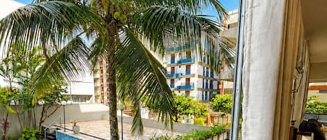 Un balcón con vista a una piscina, palmeras y un edificio de varios pisos.