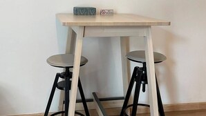 Una mesa con dos taburetes, un cartel de 'NO FUMAR' y dos cuadros abstractos en la pared.