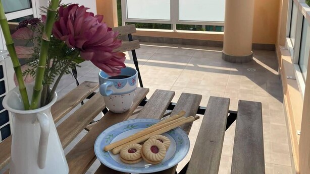 Un balcón con una mesa, un jarrón con flores y vistas a edificios.