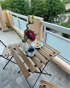 A balcony with a table set for two, featuring a vase with flowers, a plate of cookies, and a cup of coffee. - Beautiful apartment in peaceful part of Nicosia centre close to all amenities (Egkomi Lefkosias)