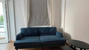 Una habitación con un sofá azul, una mesita redonda y una ventana con cortinas.