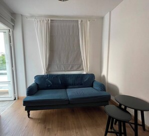Ein Zimmer mit einem blauen Sofa, einem kleinen runden Tisch und einem Fenster mit Vorhängen.