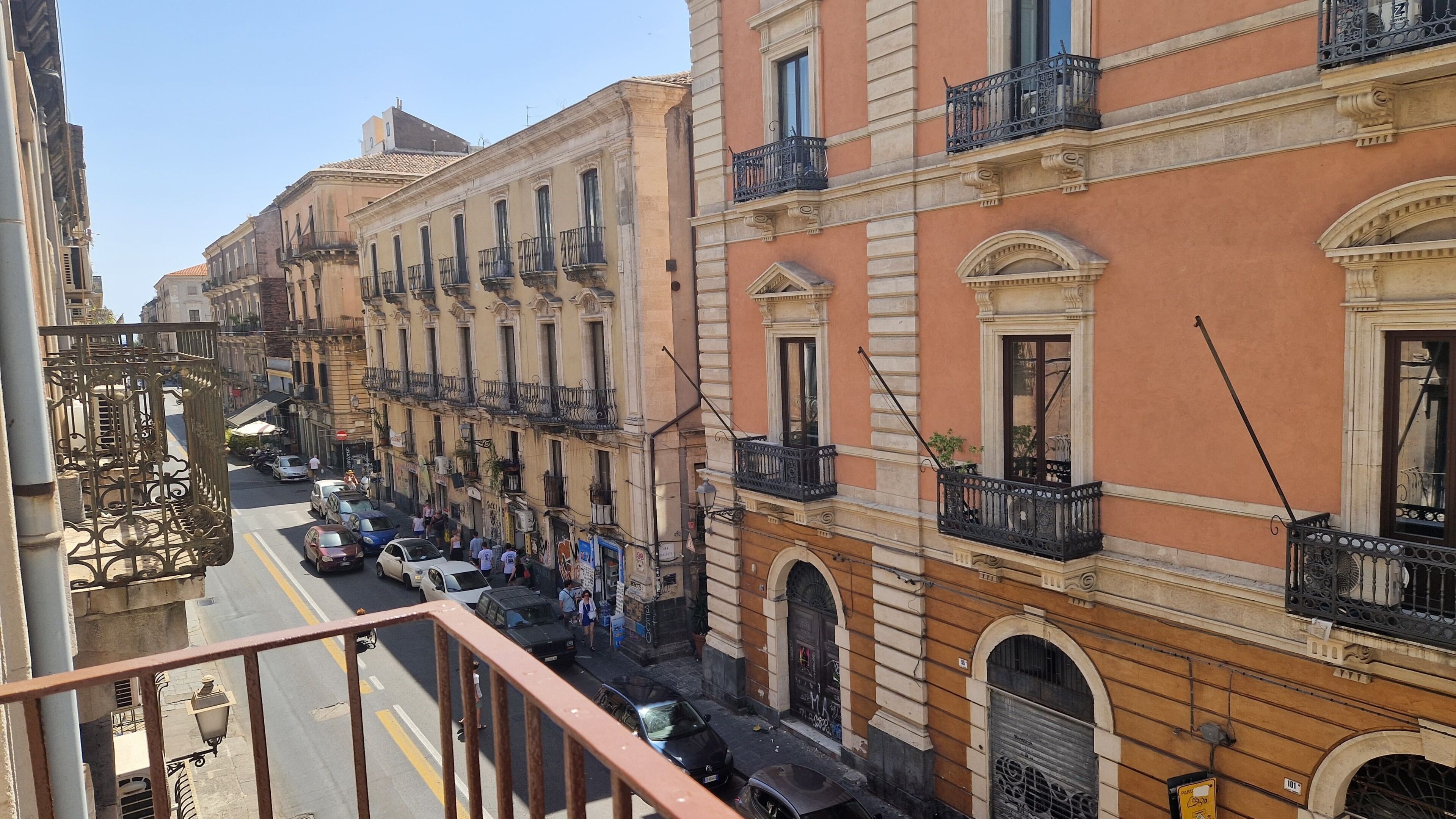 Vista de la calle con edificios de varios pisos, balcones y coches estacionados.