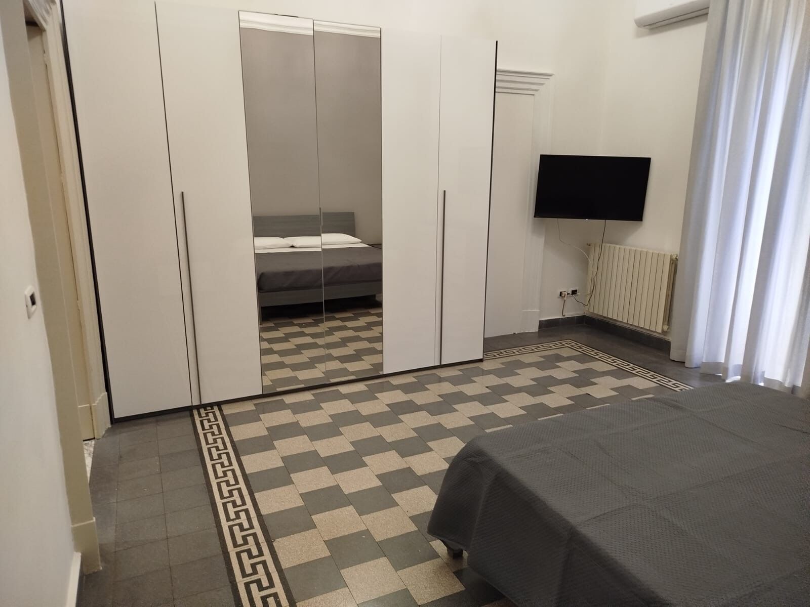 A bedroom with a bed, a wardrobe, a television, and a patterned floor.