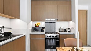 Cozinha compacta com micro-ondas, fogão e forno, armários de madeira e uma pequena tigela de frutas na bancada.
