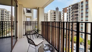 Uma varanda com cadeira e mesa de vime, com vista para uma área residencial com edifícios altos.