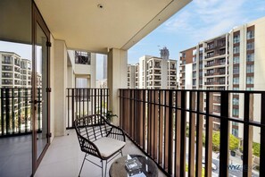 Ein Balkon mit Korbmöbeln und Tisch, mit Blick auf ein Wohngebiet mit Hochhäusern.