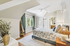 A bedroom with a large bed, a standing lamp, a window with curtains, and a view of the outdoors. - Sunset Rentals | Port Tack 67 (Hilton Head Island)