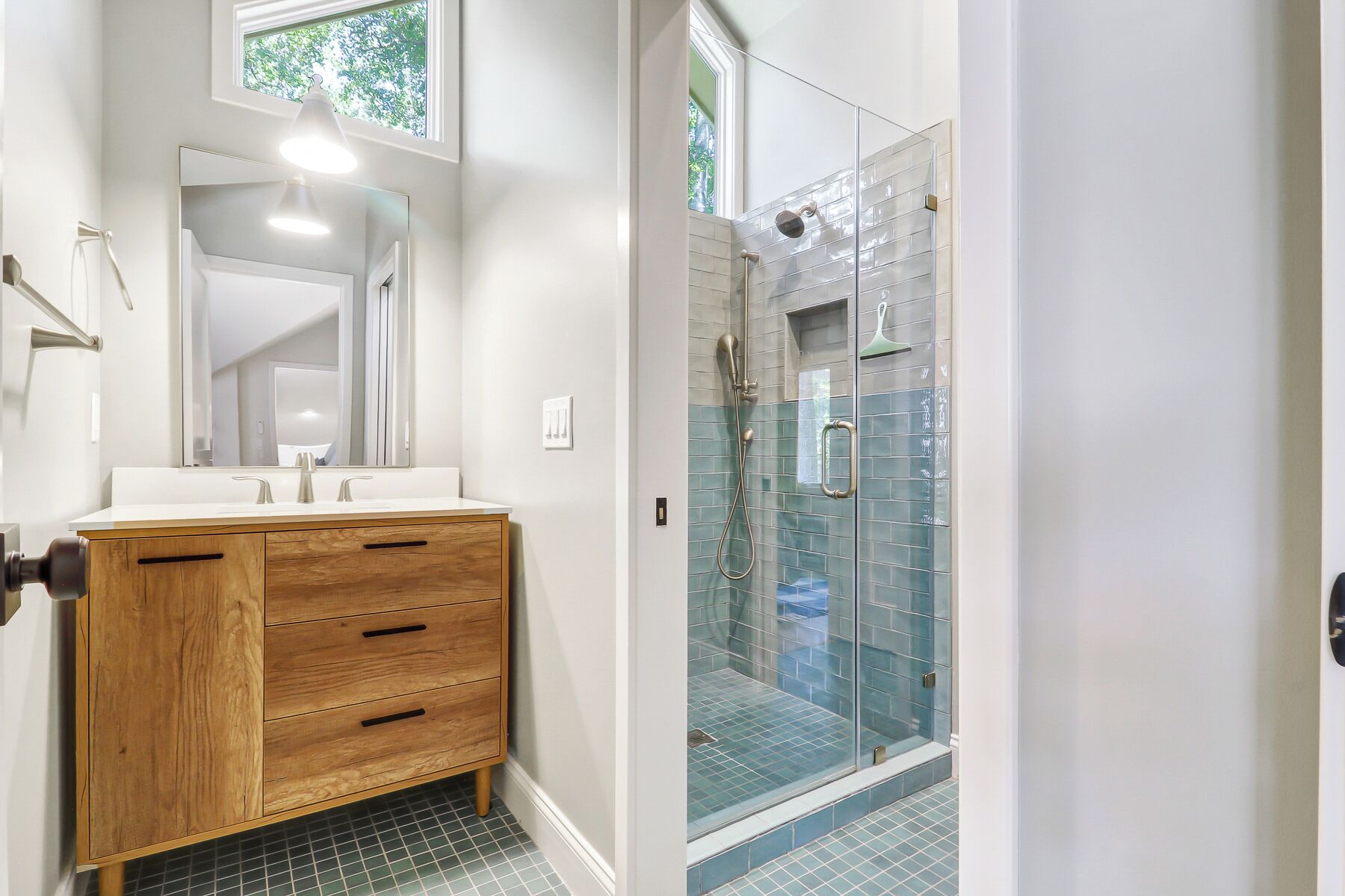 A bathroom with a wooden vanity, a mirror, a shower with glass doors, and a tiled floor.