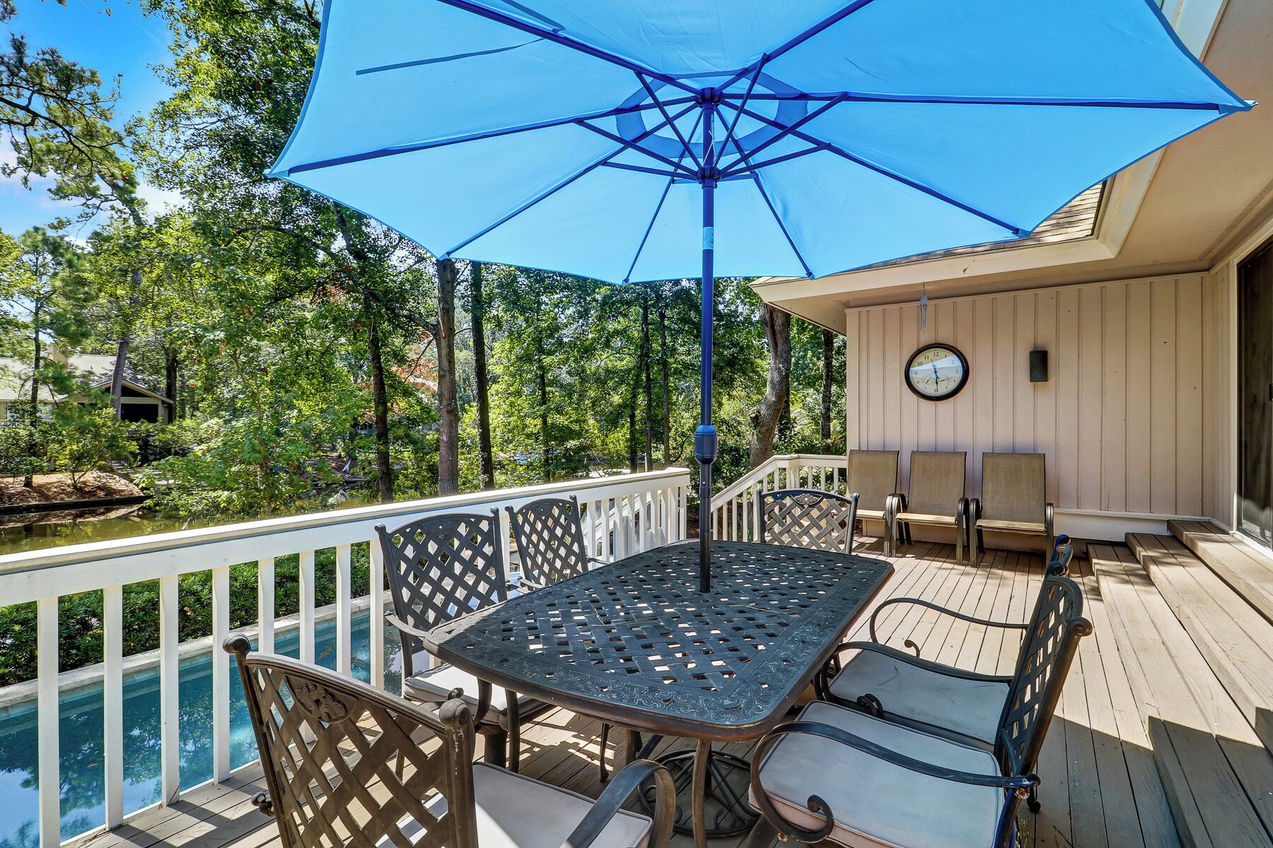 An outdoor deck with a table and chairs, a pool, and a large umbrella providing shade.