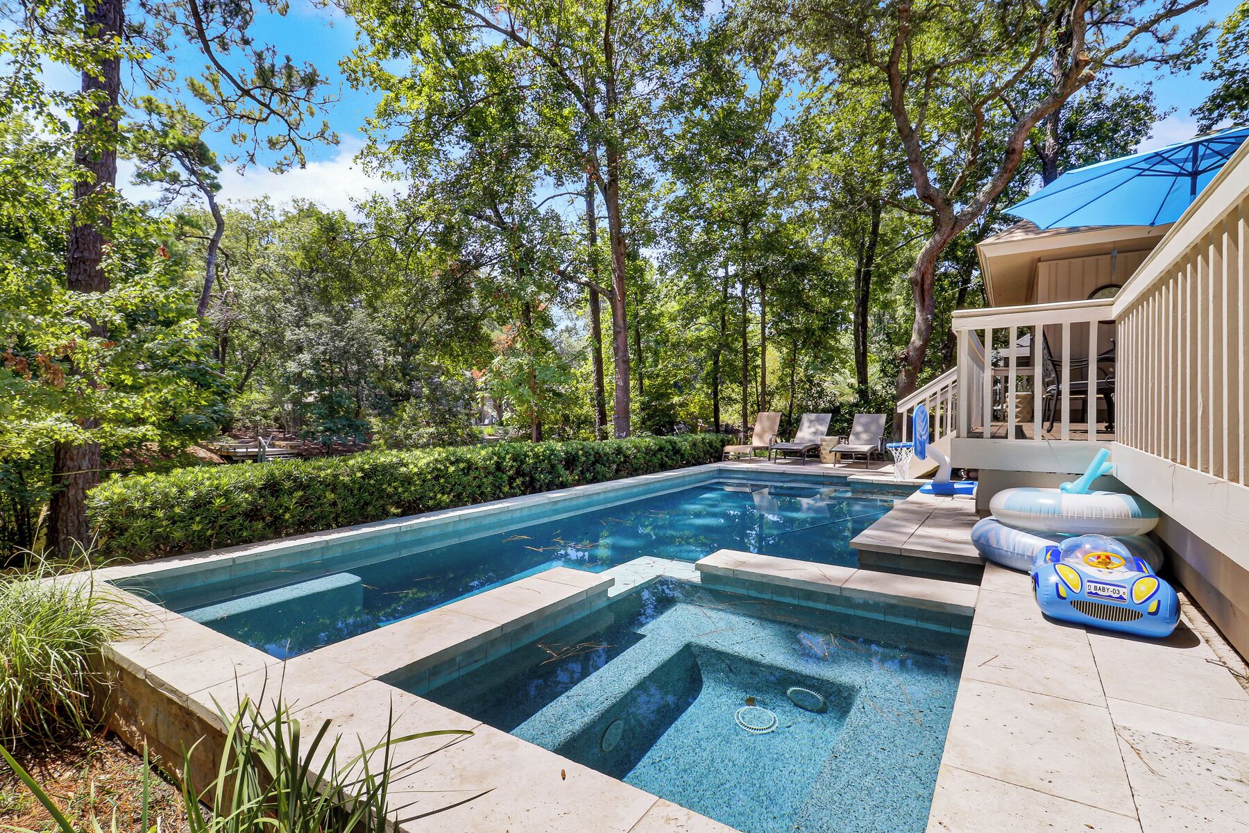 Une piscine rectangulaire divisée en deux zones distinctes, entourée d’une terrasse en bois et d’une clôture blanche.