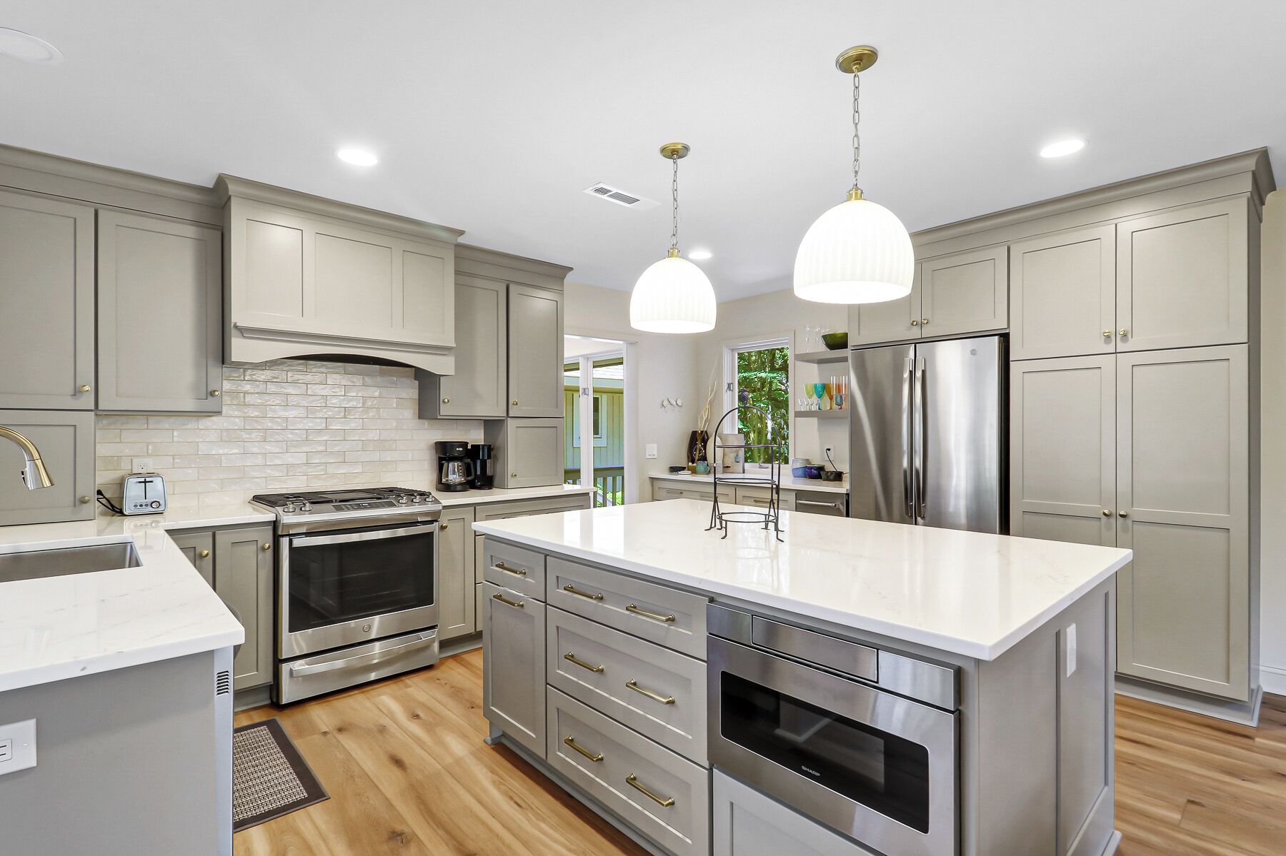 A modern kitchen with stainless steel appliances, grey cabinetry, and pendant lighting.