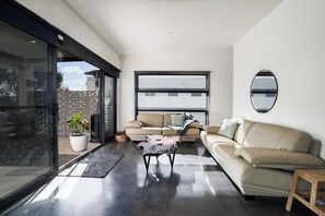 A modern living room with a glass door leading to an outdoor area, a beige sofa, a coffee table, and a large window providing natural light.