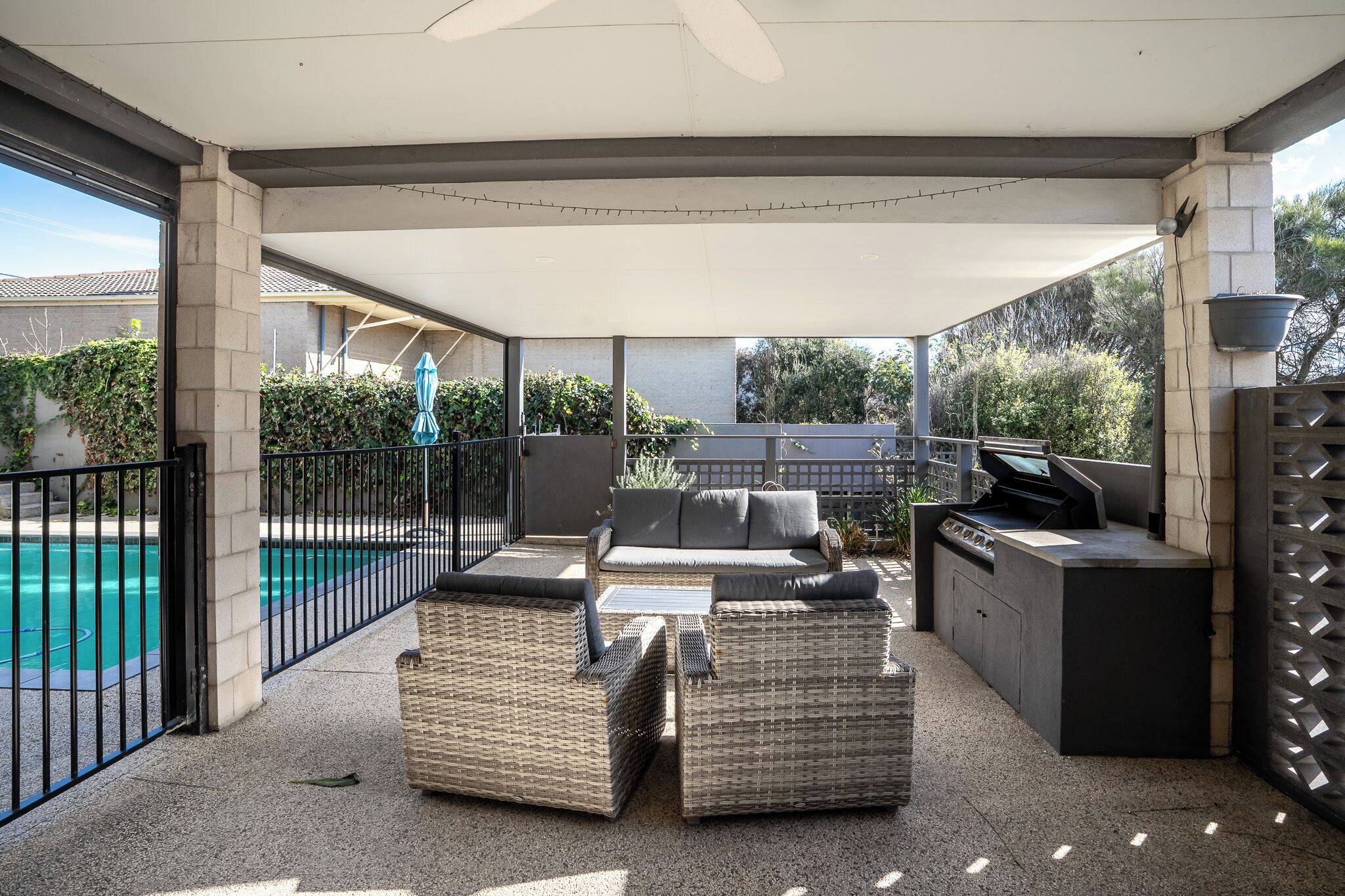 An outdoor patio with a pool, wicker furniture, and a barbecue grill.