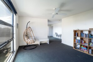 A modern room with a large window, a ceiling fan, a hanging chair, a bookshelf, and a small table.