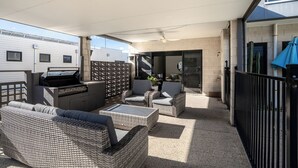 A covered outdoor patio with wicker furniture, a barbecue grill, and a view of the building's exterior. - Pool, Across from the Beach, Pet Friendly Home (Ocean Grove)