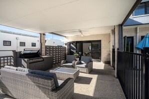Eine überdachte Terrassengrundstück mit Korbmöbeln, einem Grill und Blick auf die Außenfassade des Gebäudes.