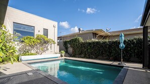 A swimming pool with a tiled deck, surrounded by a low hedge and a building with a tiled roof. - Pool, Across from the Beach, Pet Friendly Home (Ocean Grove)