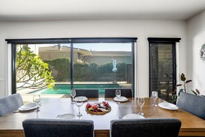 A dining area with a table set for four, overlooking a swimming pool and a garden.