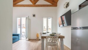 A modern kitchen with a wooden ceiling, a dining area with white chairs, and a blue sofa. - Estay - Lovely Marina Roof (Cagliari)