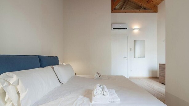 A bedroom with a bed, a blue headboard, a white wall, an air conditioning unit, and a small mirror. - Estay - Lovely Marina Roof (Cagliari)