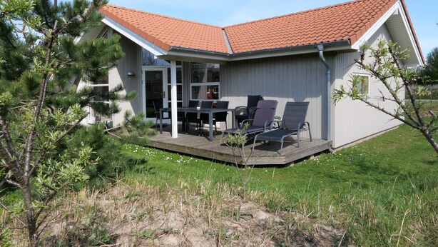 Una casa con un portico coperto, un'area pranzo con sedie e un piccolo giardino.