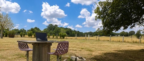 Mesa de madera al aire libre con una computadora portátil, dos sillas y un sendero de concreto.