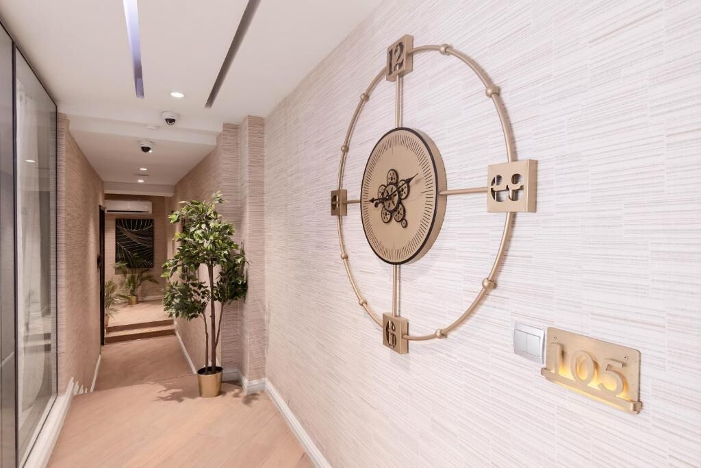 Un pasillo con un reloj en la pared, una planta en maceta e interruptor de luz.