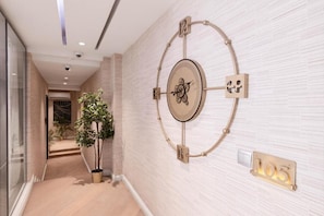 A hallway with a wall-mounted clock, a potted plant, and a light switch. - Yellow Trumpet Iris Maitama (Abuja)