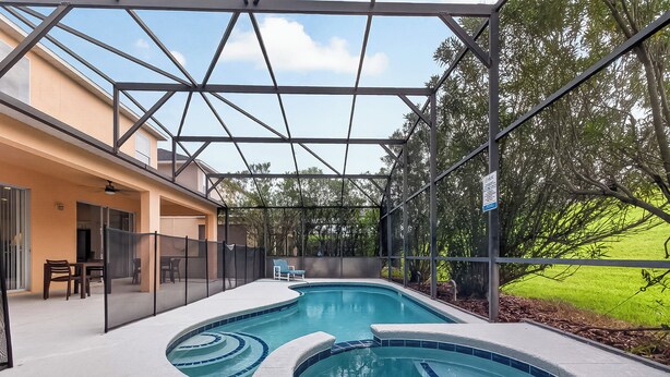 Ein Pool mit geschwungener Form, umgeben von einer überdachten Terrasse mit Sitzgelegenheiten und Blick auf eine grüne Landschaft.