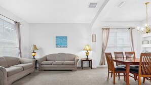 Ein Wohnzimmer mit einer Couch, einem Esstisch mit Stühlen, einer Lampe und einem Gemälde an der Wand.